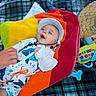 baby, infant, child, smiling, happy, portrait, lying_down, hat, white_hat, colorful_blanket, plaid_blanket, baby_clothing, ocean_theme, fish_pattern, toy, playmat, adult_hand, outdoor, close_up, family