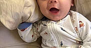 Archie is registered to the contest to win money with this photo: baby, infant, child, portrait, smiling, happy, eyes, face, lying_down, pajamas, onesie, clothing, bed, pillow, bedding, indoors, close_up, cozy, hand, photography