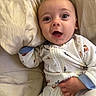 baby, infant, child, portrait, smiling, happy, eyes, face, lying_down, pajamas, onesie, clothing, bed, pillow, bedding, indoors, close_up, cozy, hand, photography