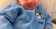 Alaina is registered to the contest to win money with this photo: baby, child, smiling, blue_sweater, cartoon, cute, infant, pillow, cozy, portrait, clothing, happy, young, indoors, person, soft, relaxed, face, skin, hand