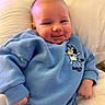 baby, child, smiling, blue_sweater, cartoon, cute, infant, pillow, cozy, portrait, clothing, happy, young, indoors, person, soft, relaxed, face, skin, hand