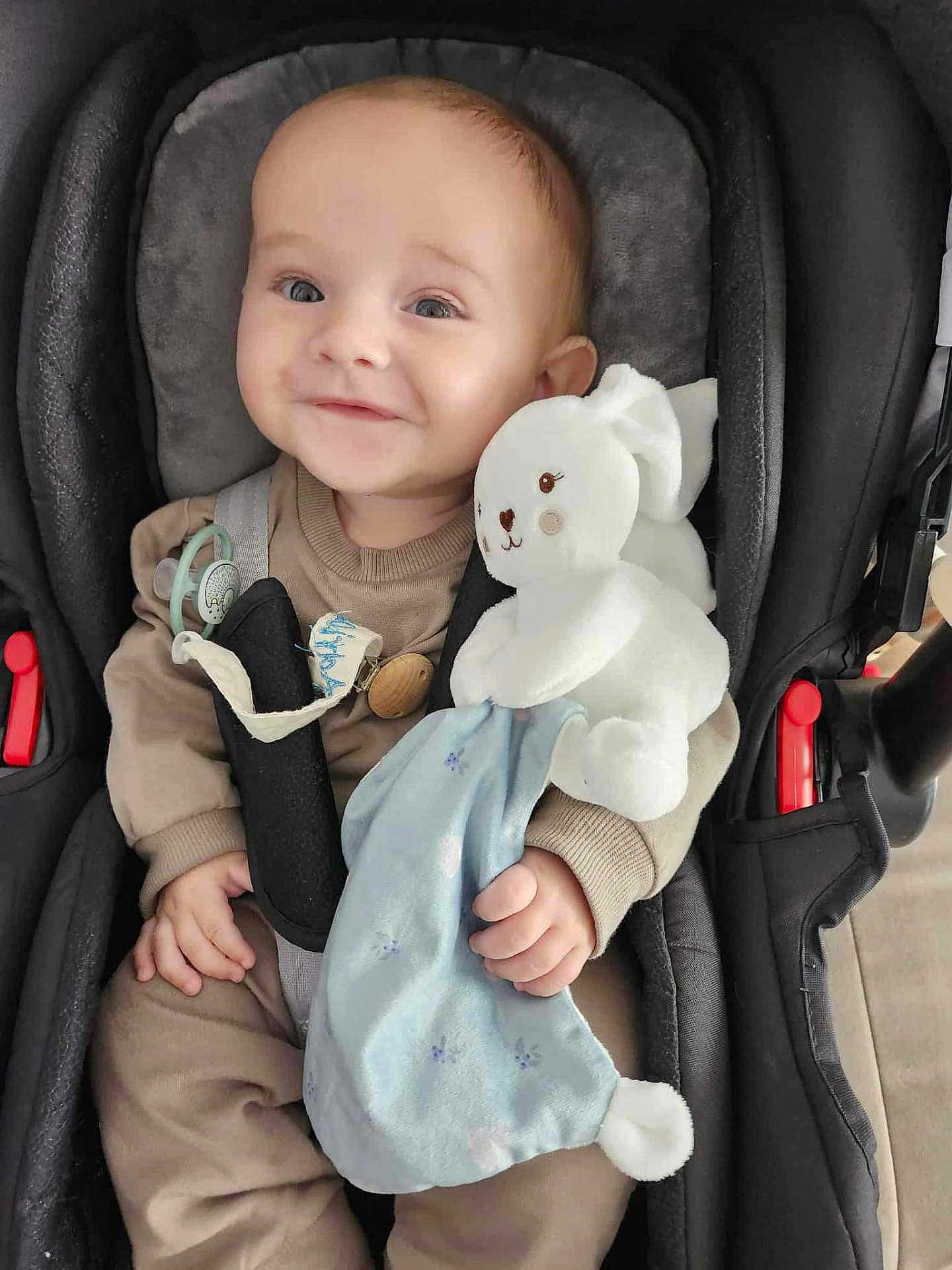 Adriann a rejoint le concours — aidez-le/la à gagner de superbes lots ! baby, infant, smiling, car_seat, plush_toy, stuffed_bunny, pacifier, safety_belt, buckle, blue_blanket, hand, adorable, portrait, cozy, seat_padding, soft_toy, clothing, infant_outfit, eyes, cute