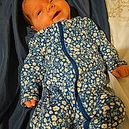 Aurora is registered to the contest to win money with this photo: baby, bed, bedding, blanket, blue, clothing, cute, face, floral_pattern, hands, infant, lying_down, newborn, onesie, person, portrait, sleepwear, soft, toddler, warm