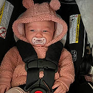 Charlotte is registered to the contest to win money with this photo: baby, infant, car_seat, pacifier, hoodie, pink_clothing, striped_pants, child, cute, safety_harness, indoor, seatbelt, warning_label, clothing, face, hand, person, closeup, portrait, cozy
