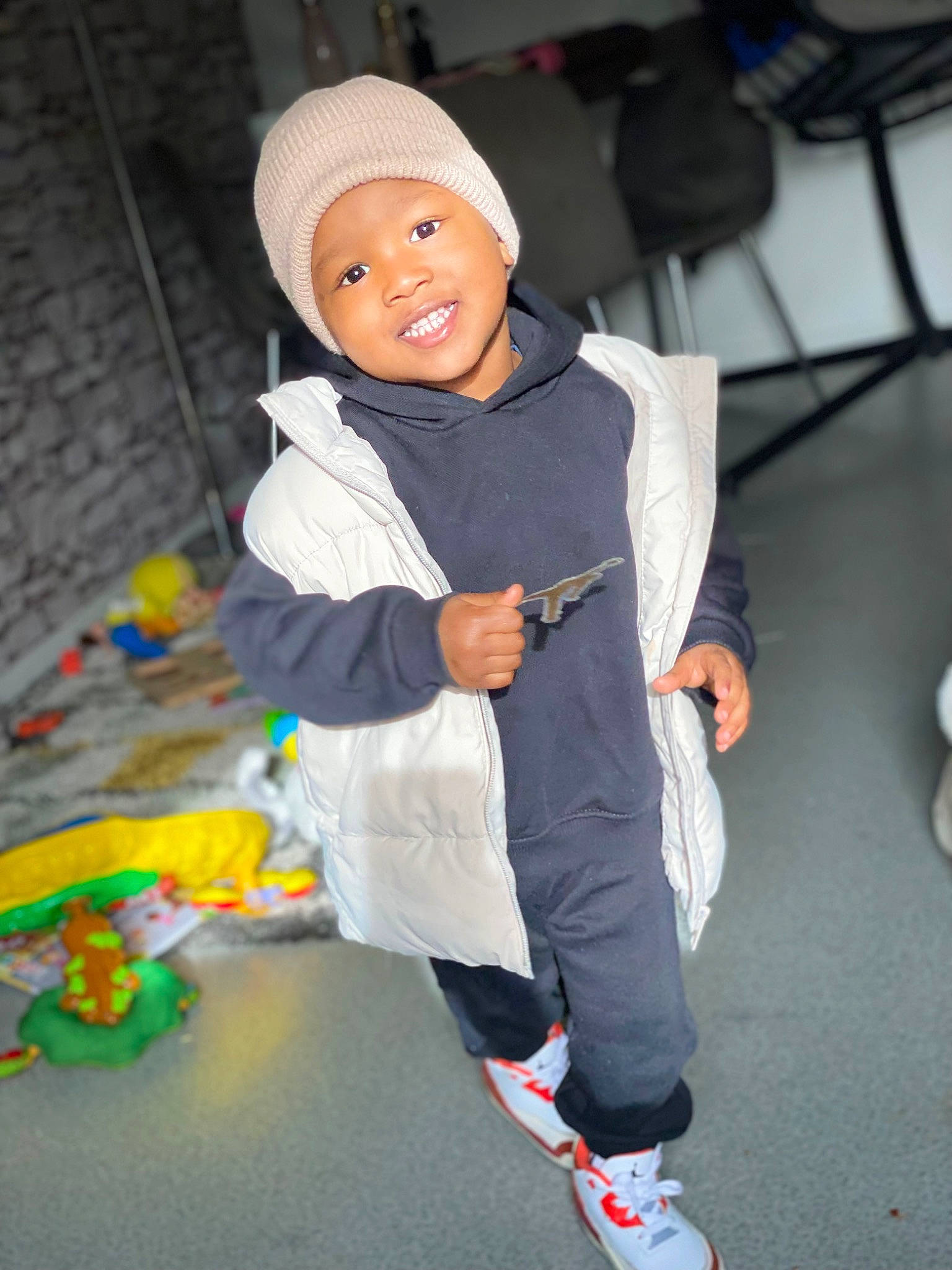 Khalil participe au concours pour gagner de l'argent avec cette photo : baby, beanie, cap, child, costume, face, flooring, fun, happy, headwear, hoodie, knee, leisure, person, personal_protective_equipment, room, sitting, sleeve, smile, sportswear