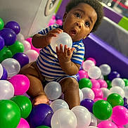Zymere is registered to the contest to win money with this photo: baby, child, play_area, plastic_balls, striped_onesie, curious, sitting, indoor, colorful, toys, fun, cute, expression, person, head, face, hand, foot, soft_lighting, background_blur