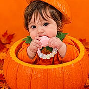 Marcela joined the competition — help win amazing prizes! baby, child, pumpkin, halloween, autumn, orange, costume, pumpkin_hat, portrait, sitting, teether, toy, smiling, face, brown_hair, infant, leaves, seasonal, studio_photography, cute