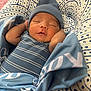 baby, newborn, sleeping, hat, blue_clothing, striped_onesie, blanket, cushion, pattern, indoor, peaceful, infant, resting, wrapped, soft_texture, cute, child, portrait, cozy, sleep