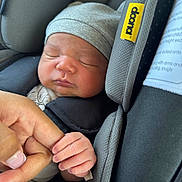 Kazan is registered to the contest to win money with this photo: newborn, baby, sleeping, car_seat, hat, hand, finger, close_up, infant, child, cozy, soft, gray, rest, cute, tenderness, family, bond, comfort, peaceful