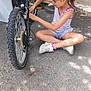 Maidie a rejoint le concours — aidez-le/la à gagner de superbes lots ! child, girl, bicycle, outdoor, pavement, sunlight, hair_clip, white_shoes, shorts, tank_top, sitting, cross_legged, repair, focus, summer, casual_clothing, toy, greenery, building, daytime