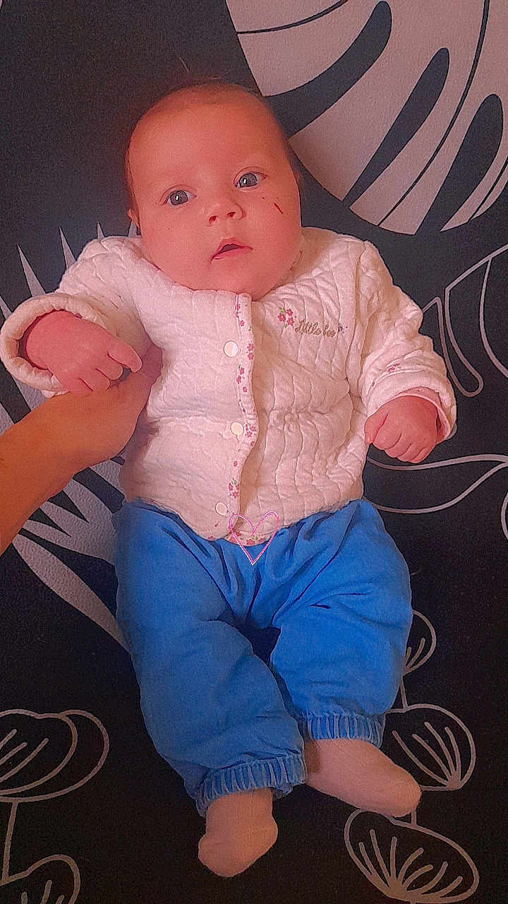 Haneïa a rejoint le concours — aidez-le/la à gagner de superbes lots ! baby, infant, child, white_jacket, blue_pants, sock, hand, face, eyes, scratch, patterned_background, soft_lighting, portrait, cute, lying_down, clothing, skin, person, indoor, holding_hand