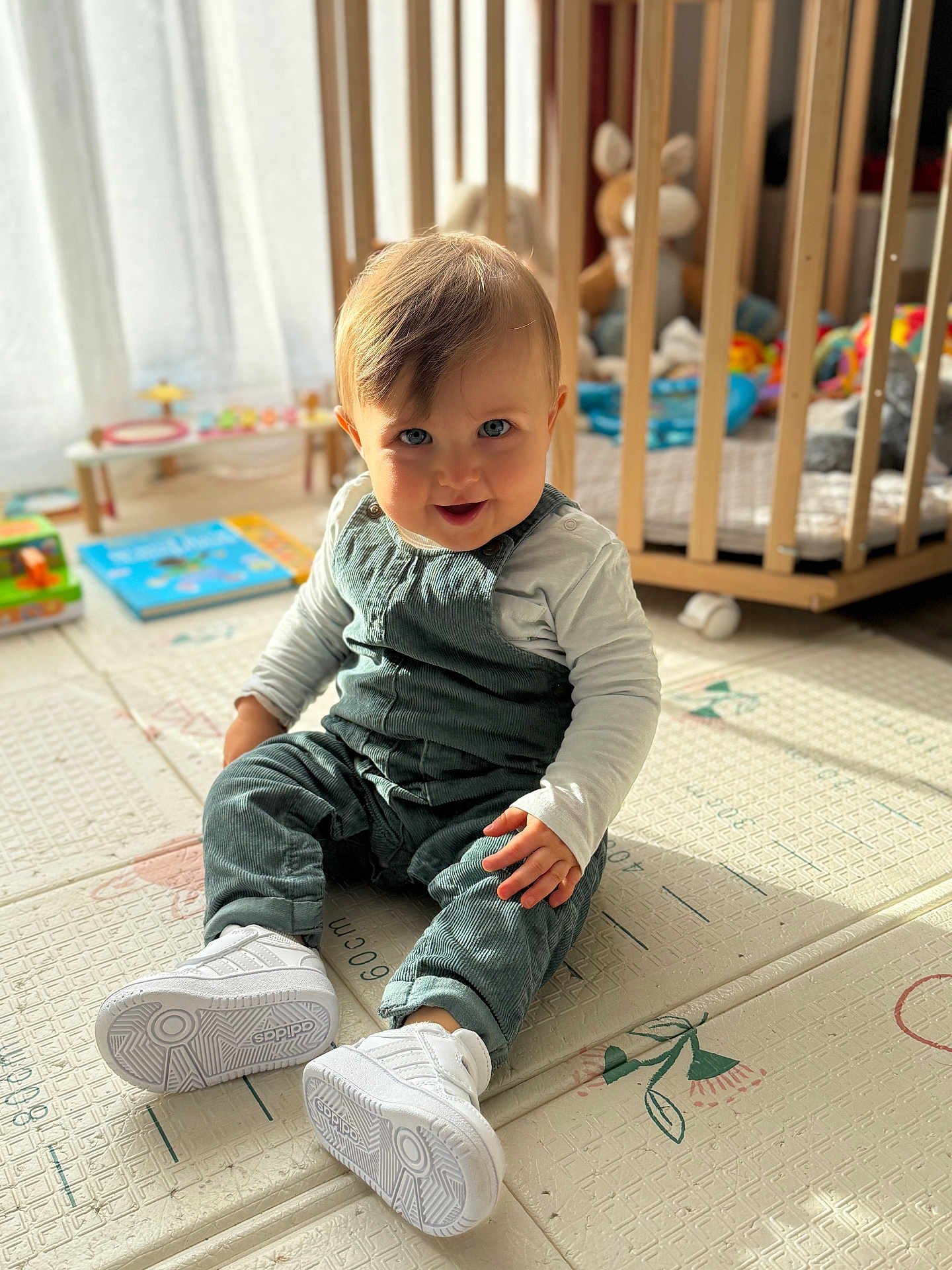 Jules participe au concours pour gagner de l'argent avec cette photo : baby, child, infant, blue_eyes, overalls, white_shoes, play_mat, nursery, crib, toys, indoor, smiling, sitting, cute, soft_light, wooden_furniture, floor, happy, portrait, young_child
