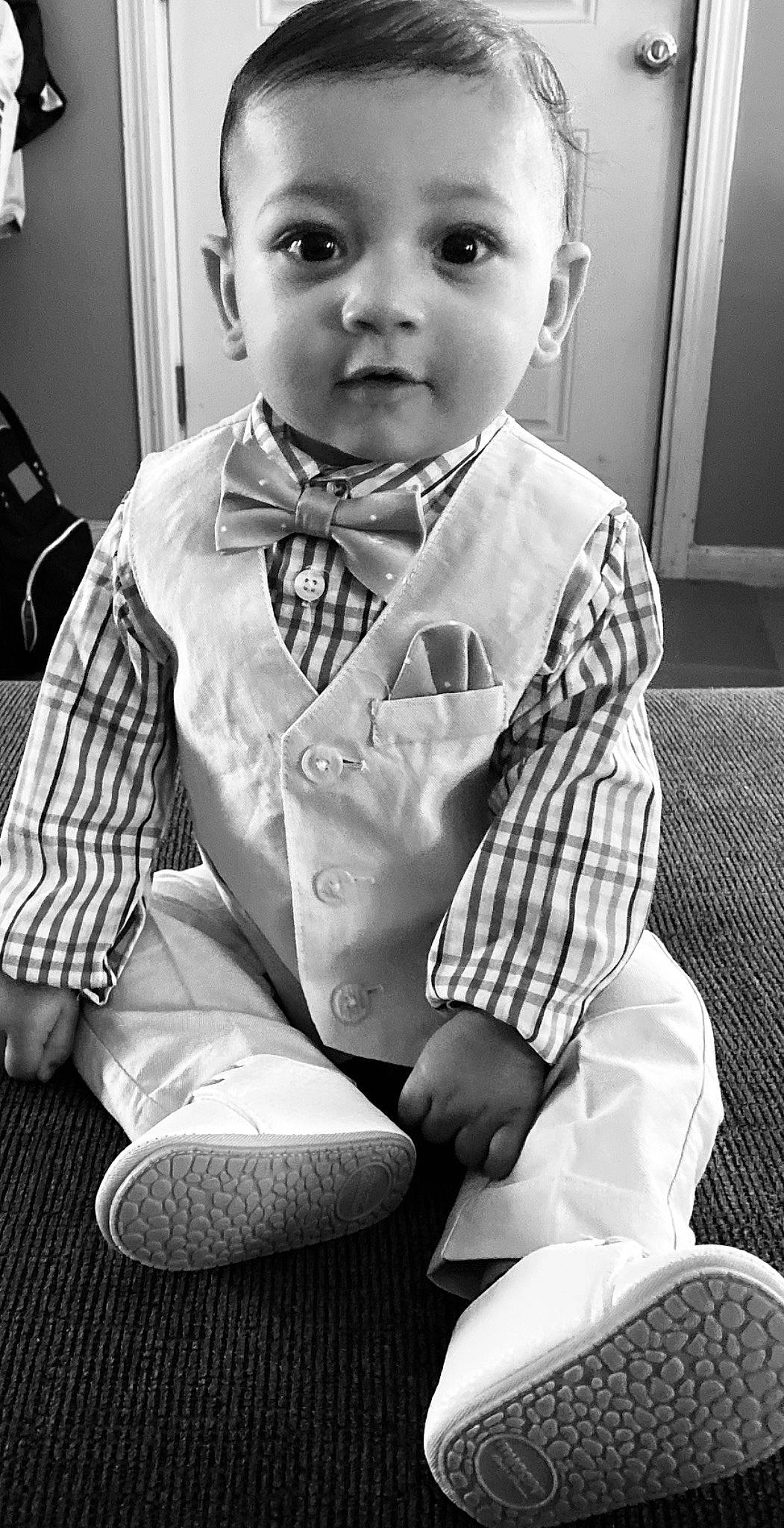 Boston is registered to the contest to win money with this photo: baby, black, black_and_white, bow_tie, child, face, formal_wear, monochrome, monochrome_photography, outerwear, person, photography, room, sitting, smile, stock_photography, suit, tie, toddler, tuxedo
