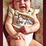 Emiliana is registered to the contest to win money with this photo: baby, child, clothing, comfortable, cushion, cute, floral_pattern, furniture, hand, happy, head, indoors, infant, onesie, person, portrait, sitting, skin, smiling, young_child