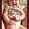 Emiliana is registered to the contest to win money with this photo: baby, child, comfort, cushion, cute, face, floral, hand, happy, indoors, infant, joy, leg, onesie, person, portrait, sitting, skin, smile, text_on_clothing