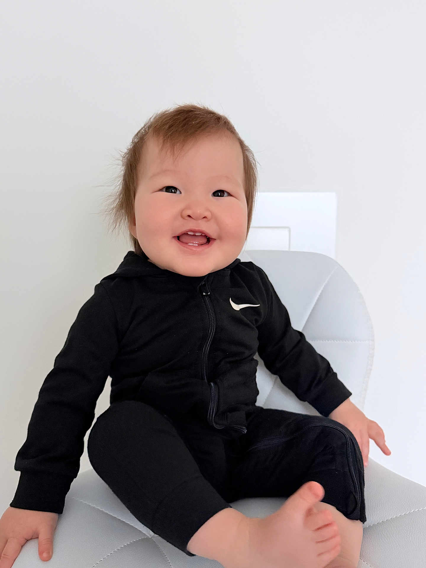 Miray Temirlan joined the competition — help win amazing prizes! baby, child, smiling, sitting, black_clothing, nike_logo, white_chair, happy, toddler, indoor, portrait, cute, foot, hand, hair, minimalist_background, face, expression, young_child, casual_wear