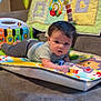 baby, infant, play_mat, toys, couch, colorful, quilt, animal_patches, indoor, child, person, cute, curious, soft_toys, baby_clothes, smiling, face, head, lying_down, home