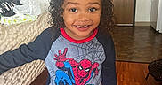 Terrance is registered to the contest to win money with this photo: child, smile, curly_hair, spiderman_shirt, indoor, wooden_floor, bed, door, person, happy, clothing, portrait, young_child, home, casual, floor, room, background, standing, bright