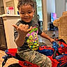 child, boy, smiling, indoor, toy_motorcycle, teenage_mutant_ninja_turtles, tshirt, camo_pants, hand_gesture, living_room, television, couch, floor, door, window, carpet, furniture, hair, person, play