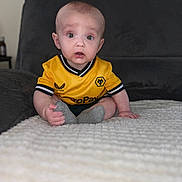 Nate is registered to the contest to win money with this photo: baby, child, infant, yellow_jersey, sitting, blanket, couch, indoor, curious, wide_eyes, short_hair, sock, portrait, person, soft_texture, casual_clothing, home, expression, cute, young