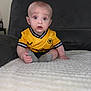 baby, child, infant, yellow_jersey, sitting, blanket, couch, indoor, curious, wide_eyes, short_hair, sock, portrait, person, soft_texture, casual_clothing, home, expression, cute, young