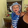 Cooper is registered to the contest to win money with this photo: baby, child, smiling, striped_clothing, striped_hat, blue_and_white, indoor, kitchen, wooden_chair, adult, holding, happy, person, face, hand, table, bottle, cabinet, appliance, portrait