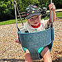 Cooper joined the competition — help win amazing prizes! toddler, child, swing, playground, cap, hat, dinosaur_print, outdoor, sunny, daylight, greenery, park, chains, woodchips, shorts, white_shirt, happy, smiling, person, legs