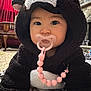baby, child, pacifier, costume, bear_costume, hood, indoors, carpet, furniture, red_curtain, living_room, cute, adorable, pink_beads, face, person, childwear, home, cozy, floor