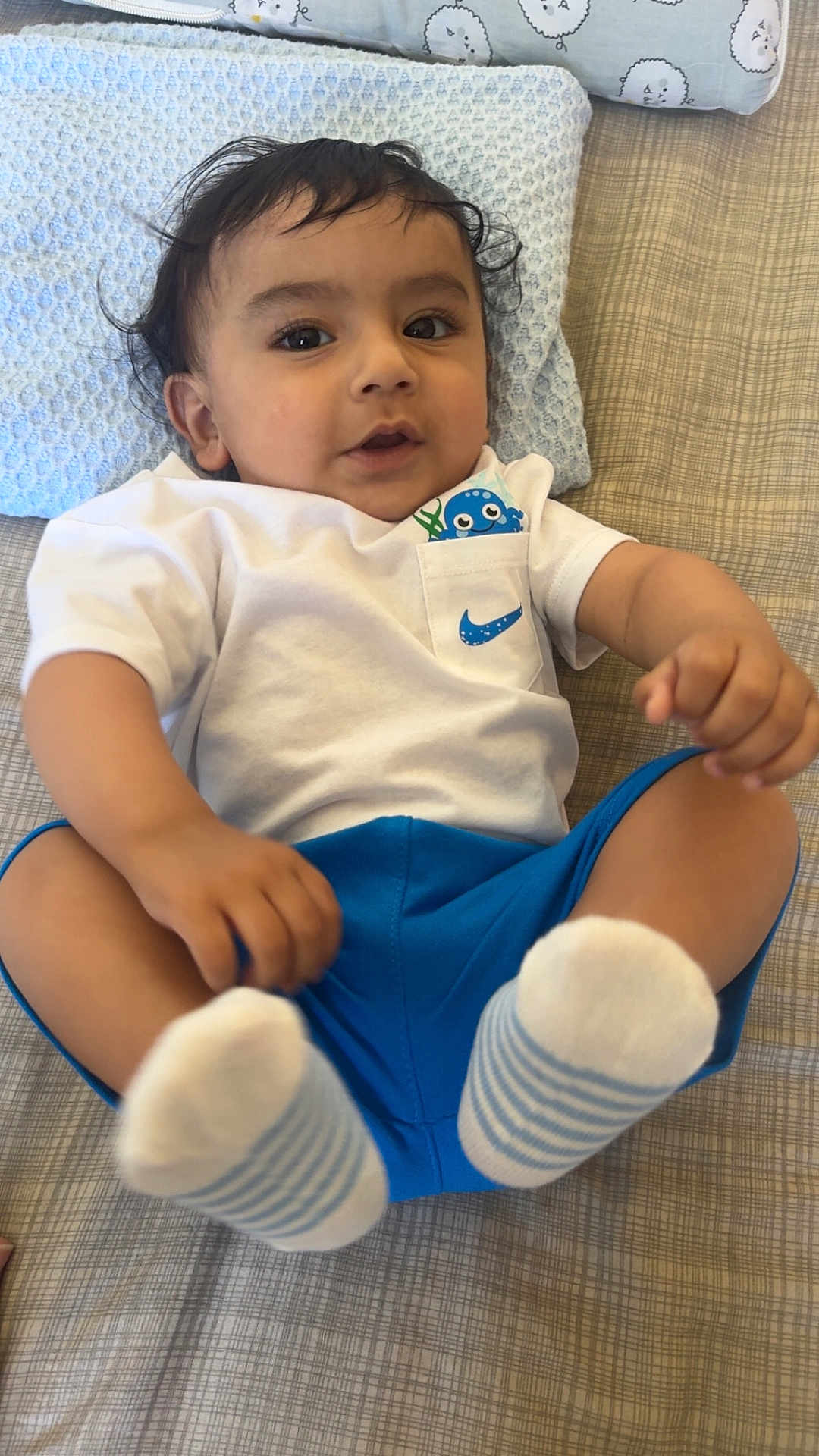 Nirvaan is registered to the contest to win money with this photo: baby, child, infant, cute, lying_down, white_shirt, blue_shorts, socks, bed, pillow, hand, footwear, face, eyes, hair, clothing, indoors, portrait, playful, curious