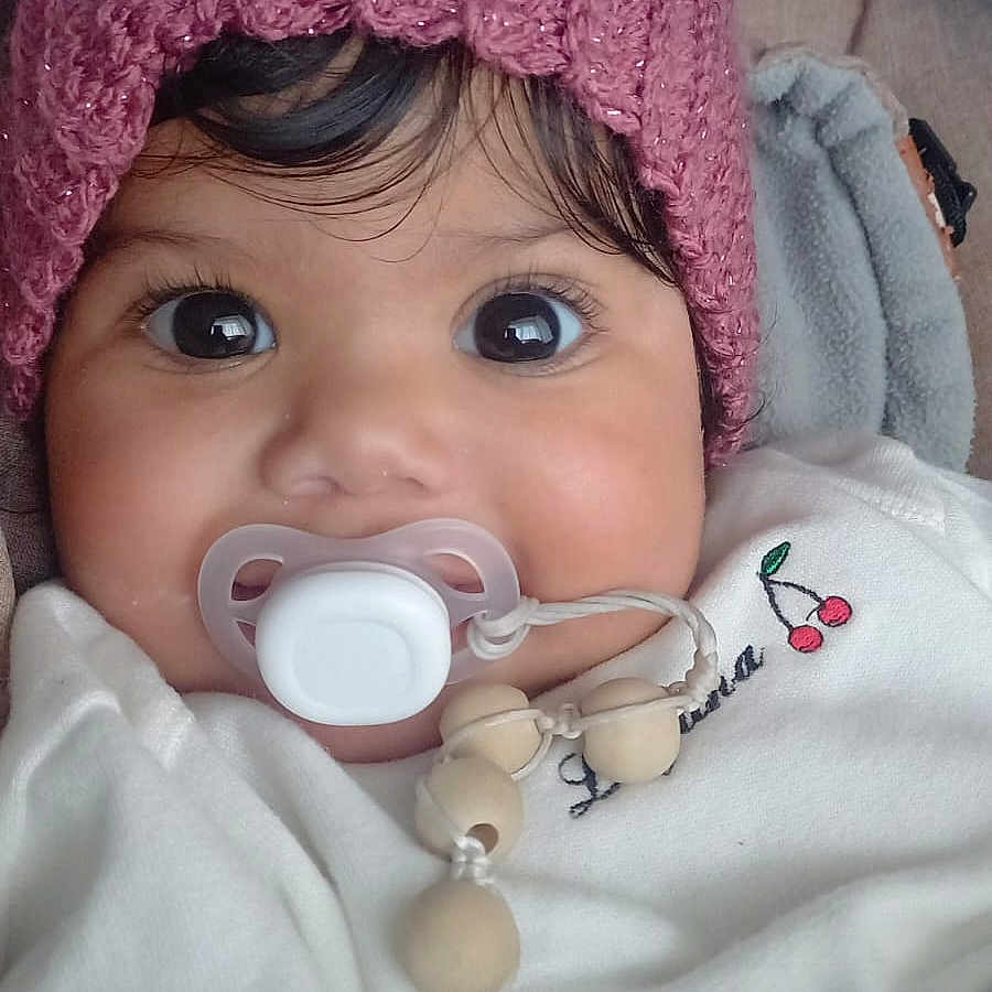 Eloah participe au concours pour gagner de l'argent avec cette photo : baby, beads, big_eyes, blanket, child, close_up, cozy, curly_hair, cute, face, indoors, infant, pacifier, pink_hat, portrait, smiling_eyes, soft_texture, toddler, warm_clothing, white_outfit
