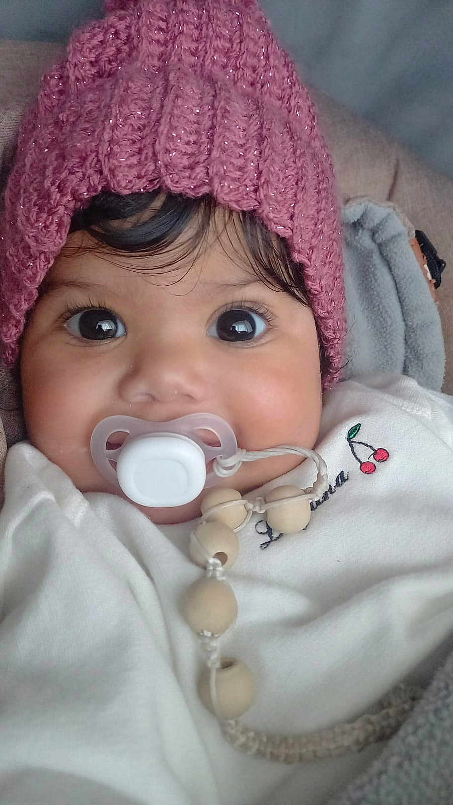 Eloah participe au concours pour gagner de l'argent avec cette photo : baby, pacifier, pink_hat, white_outfit, close_up, face, big_eyes, curly_hair, blanket, beads, cute, infant, child, indoors, soft_texture, warm_clothing, portrait, smiling_eyes, cozy, toddler