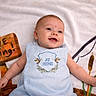 baby, infant, smiling, blue_outfit, blanket, gone_fishing_sign, fishing_rod, cattails, happy, lying_down, cute, child, portrait, playful, outdoor_theme, soft_texture, young, person, relaxing, decorative
