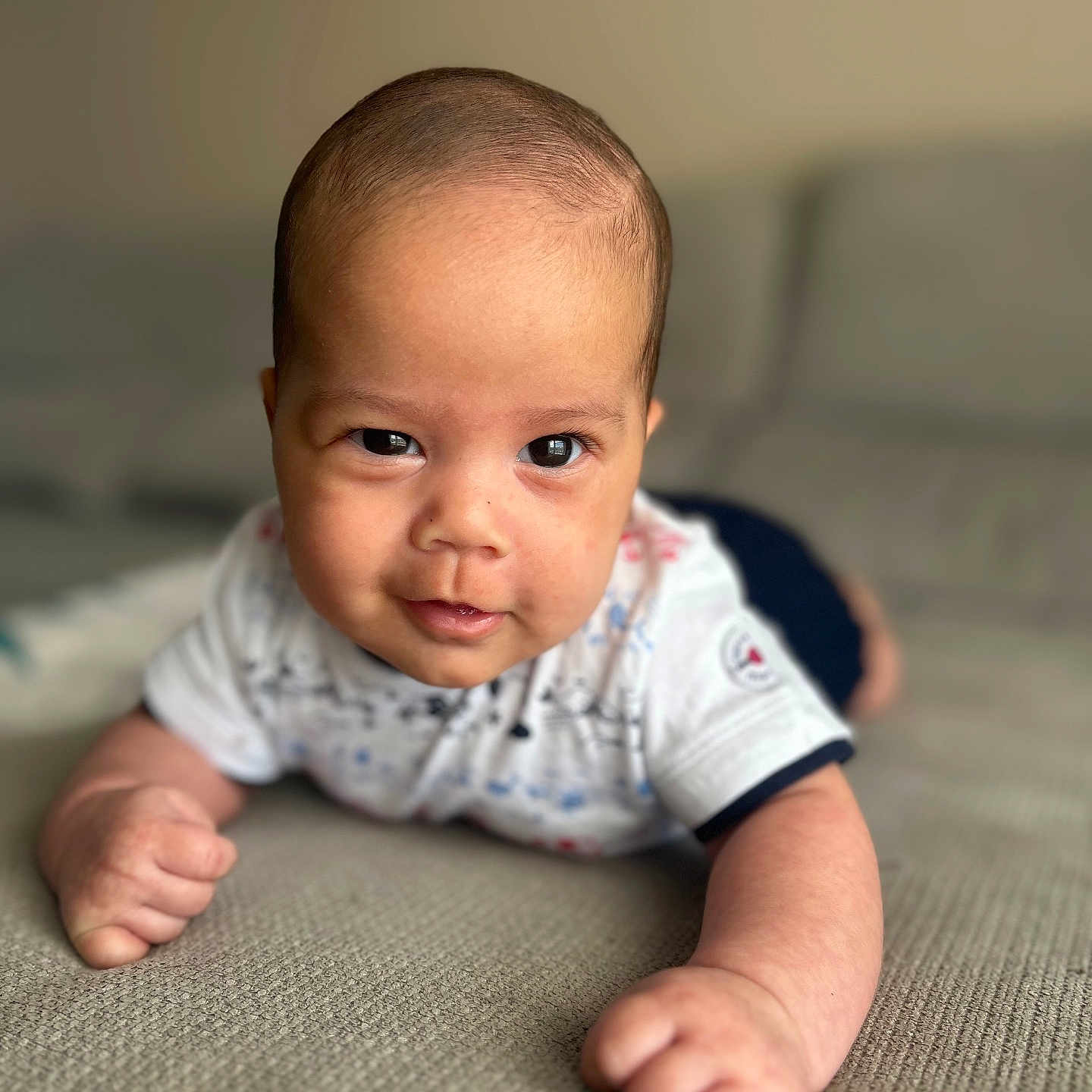 Jagath participe au concours pour gagner de l'argent avec cette photo : arms, baby, closeup, clothing, couch, cute, expression, eyes, face, head, indoor, infant, person, portrait, short_sleeves, skin, smile, textured_surface, tummy_time, young_child