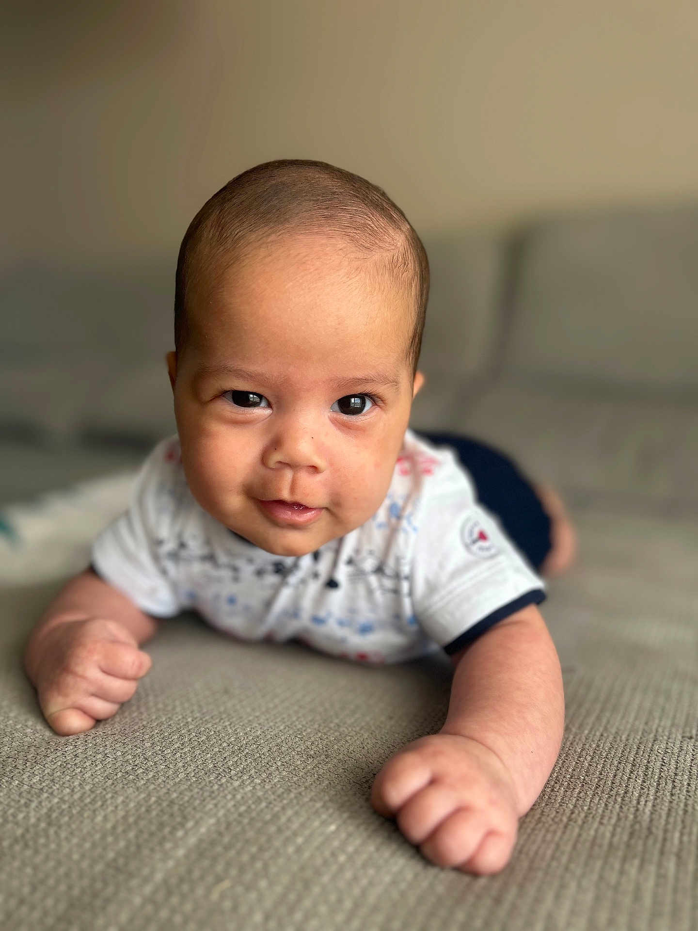 Jagath participe au concours pour gagner de l'argent avec cette photo : baby, infant, face, arms, couch, textured_surface, smile, eyes, clothing, short_sleeves, person, skin, head, indoor, portrait, cute, young_child, tummy_time, expression, closeup