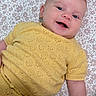 baby, infant, child, smiling, happy, portrait, lying_down, yellow_outfit, knit_clothing, floral_blanket, patterned_background, close_up, face, blue_eyes, earring, indoor, cozy, fluffy_toy, adorable, photography