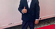 Zian a rejoint le concours — aidez-le/la à gagner de superbes lots ! child, boy, suit, thumbs_up, red_carpet, sneakers, smile, posing, outdoor, fashion, portrait, young, confident, casual, formal_wear, standing, person, hair, face, wall