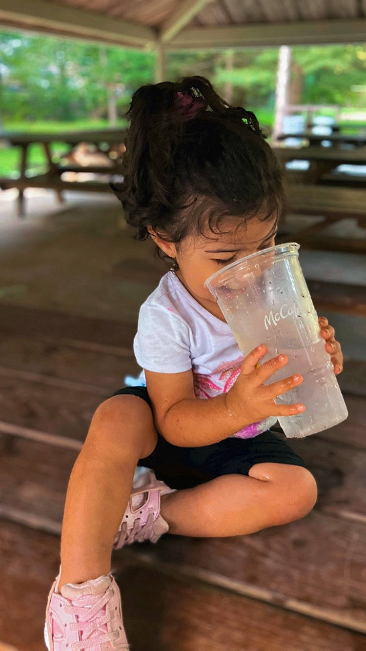 Lariaha is registered to the contest to win money with this photo: child, drink, drinking, drinkware, facial_expression, fun, glass, grass, happy, human_leg, leisure, person, recreation, sandal, shorts, sitting, soft_drink, sunglasses, thigh, toddler