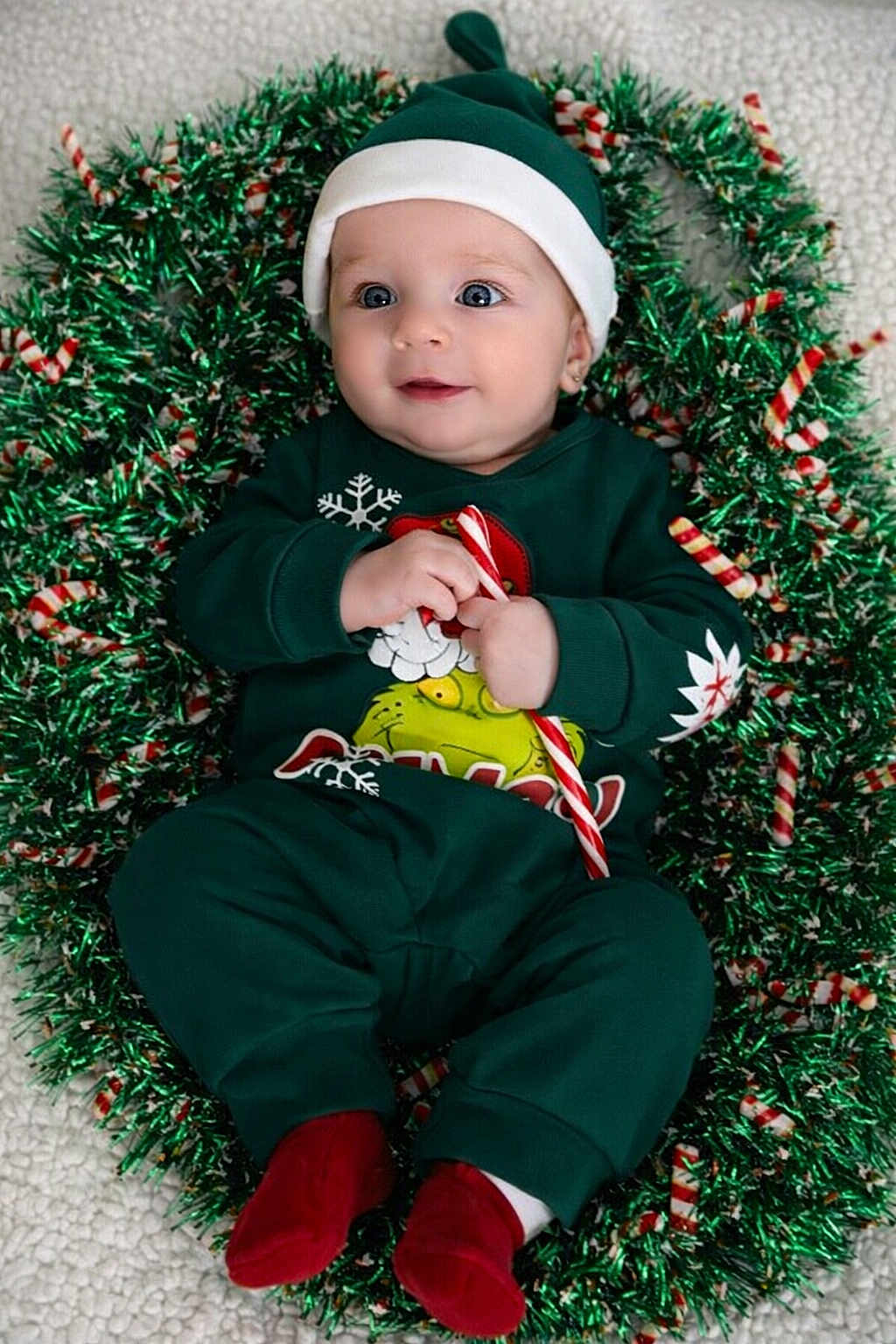Coleson is registered to the contest to win money with this photo: baby, infant, holiday, christmas, wreath, candy_cane, green_clothing, red_socks, festive, cute, smiling, face, hat, lying_down, toddler, christmas_theme, holiday_decor, child, indoors, portrait
