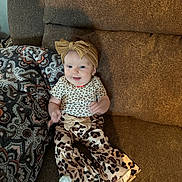 Oakley joined the competition — help win amazing prizes! baby, child, smiling, couch, blanket, headband, bow, leopard_print, clothing, pattern, infant, happy, indoor, portrait, sitting, person, cute, fashion, playful, cozy
