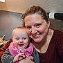 Sylvia is registered to the contest to win money with this photo: baby, woman, smile, hug, indoors, pink_bib, watch, joyful, happy, casual_clothing, person, face, portrait, head, skin, human, furniture, lamp, couch, home