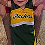 toddler, child, smiling, person, indoor, carpet, barefoot, hands, holding, red_clothing, green_bay_packers, sportswear, cheerleader_outfit, feet, adult, happy, young, standing, family, casual