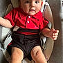 arms, baby, baby_carrier, black_shorts, casual_clothing, child, comfortable, curious, cushion, eyes, face, indoors, infant, legs, looking_at_camera, mouth, red_shirt, seatbelt, short_sleeves, skin