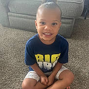 Anylah is registered to the contest to win money with this photo: barefoot, blue_shirt, carpet, chair, child, curly_hair, cute, furniture, hair_tie, happy, home, indoor, person, portrait, shorts, sitting, smiling, text_on_shirt, window_light, young