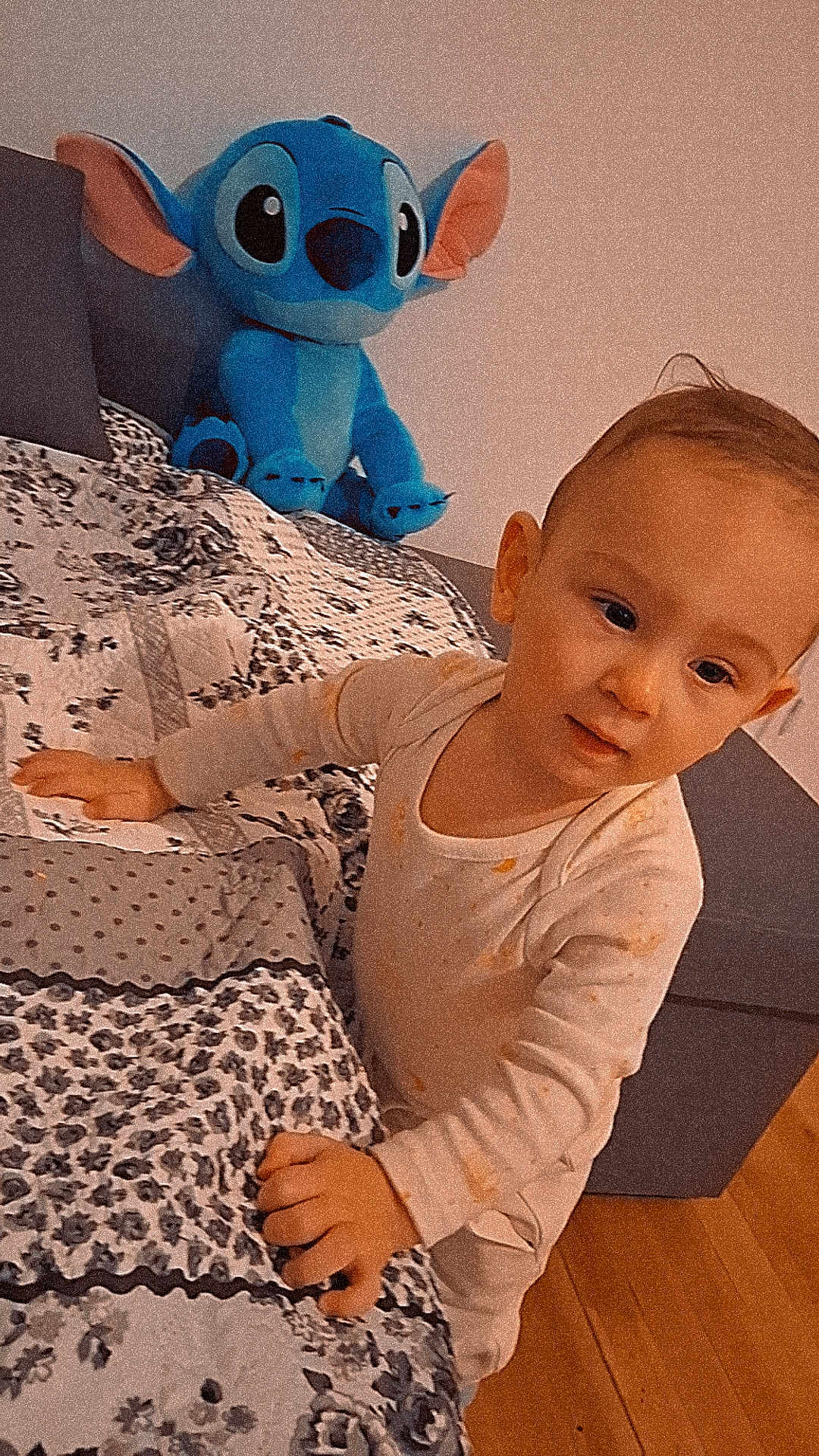 Mathias Nicolas participe au concours pour gagner de l'argent avec cette photo : toddler, child, bed, plush_toy, stitch, pajamas, indoor, carpet, wood_floor, patterned_bedspread, curious, leaning, hand, face, smiling, toy, blue, ear, couch, home
