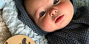Luca is registered to the contest to win money with this photo: baby, infant, four_months, blanket, knitwear, blue_eyes, face, portrait, cozy, cute, wooden_plaque, milestone, soft_texture, laying_down, indoors, child, newborn, head, expression, warm