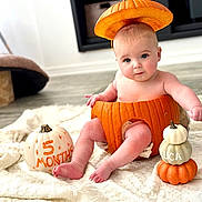 Luca is registered to the contest to win money with this photo: baby, pumpkin, orange, blanket, floor, hand, decor, cute, infant, autumn, holiday, fall, sitting, costume, headwear, skin, foot, toes, indoor, celebration