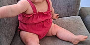 Remi-Mae joined the competition — help win amazing prizes! baby, child, romper, red_clothing, couch, sofa, indoor, curious, blue_eyes, hair_clip, infant, person, furniture, sitting, legs, arm, home, portrait, casual, relaxed