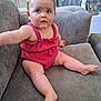 baby, child, romper, red_clothing, couch, sofa, indoor, curious, blue_eyes, hair_clip, infant, person, furniture, sitting, legs, arm, home, portrait, casual, relaxed