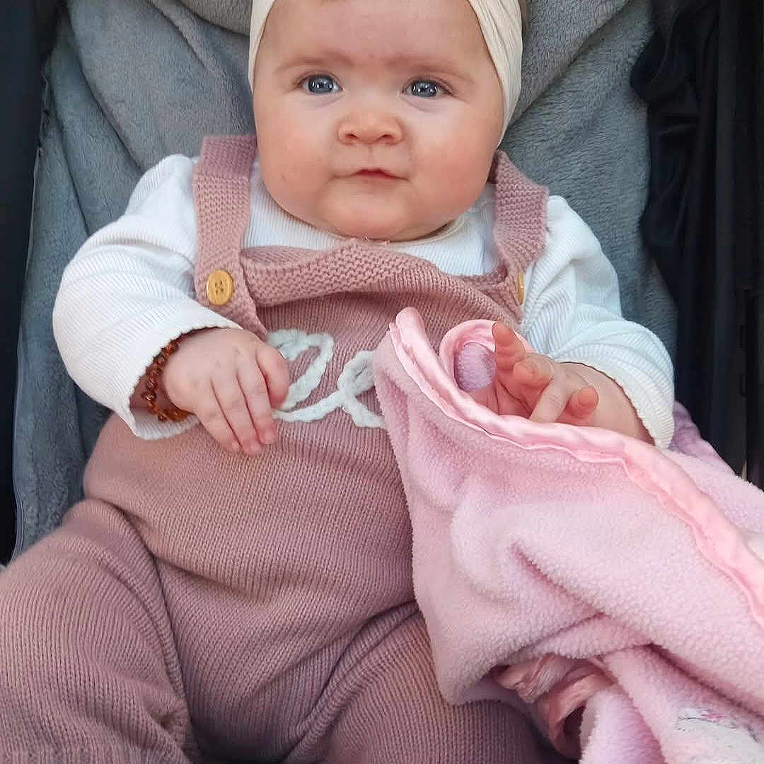 Remi-Mae is registered to the contest to win money with this photo: baby, blanket, bow, child, comfort, cozy, cute, eyes, face, hands, headband, indoors, infant, knitwear, pink_blanket, portrait, sitting, soft_texture, white_shirt, young_child