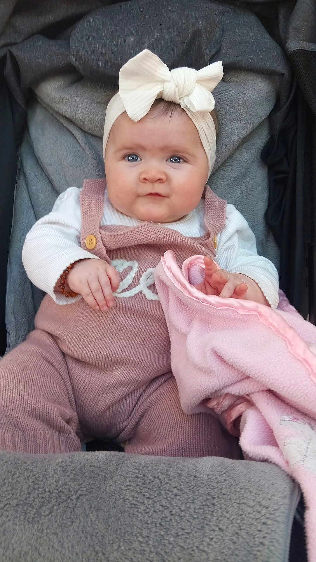 Remi-Mae is registered to the contest to win money with this photo: baby, infant, child, pink_blanket, headband, bow, knitwear, white_shirt, cute, sitting, blanket, soft_texture, portrait, indoors, comfort, young_child, face, eyes, hands, cozy